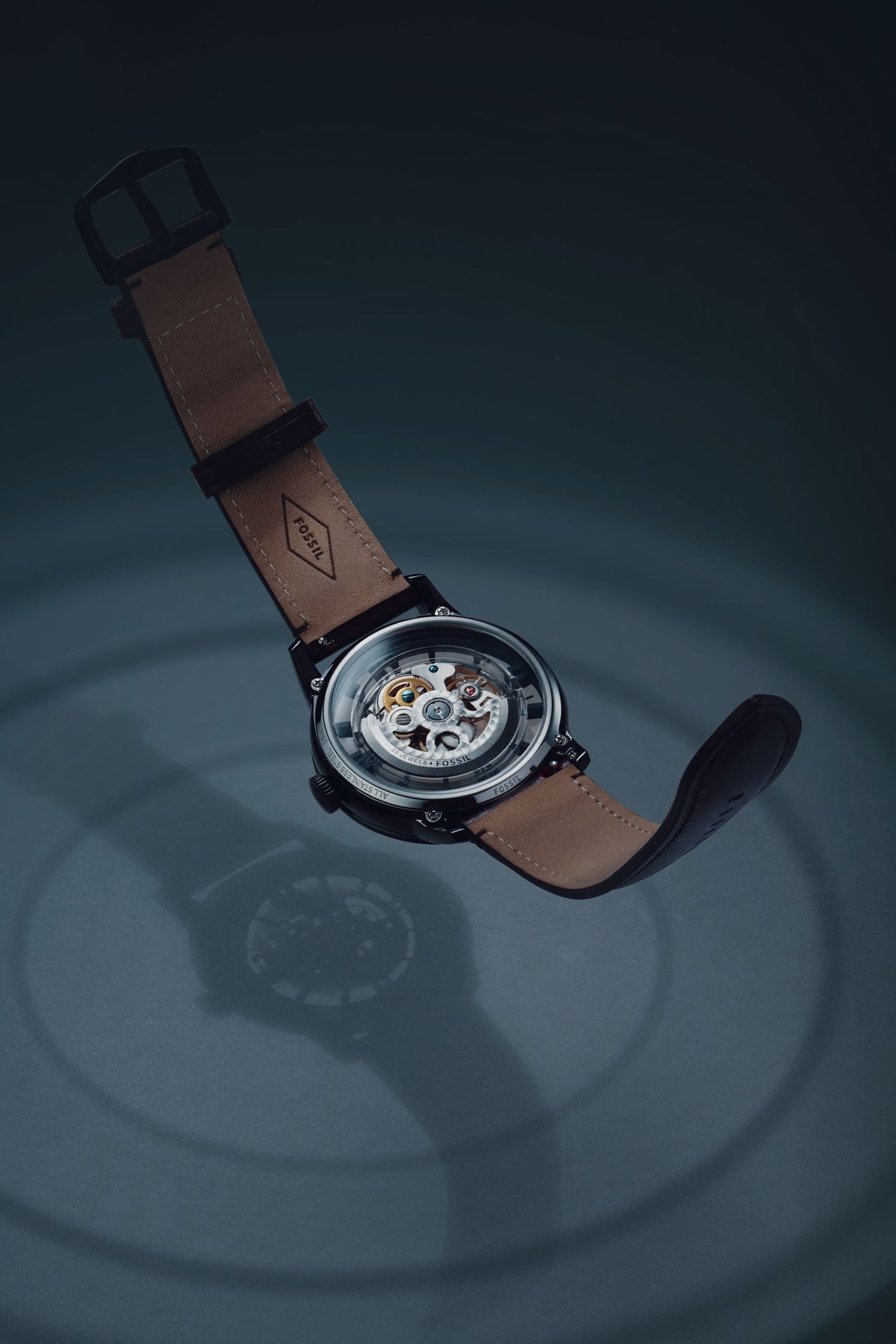 Fossil watch suspended in mid-air with concentric circle shadows on the backdrop, emphasizing the mechanical details and precision of the watch design.