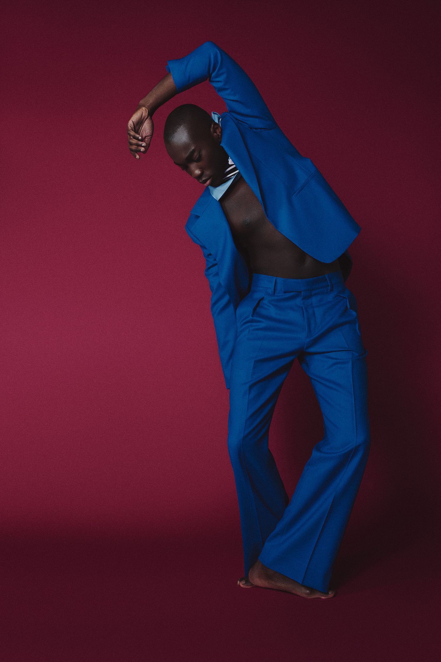 a man in a blue suit is posing in front of a red background