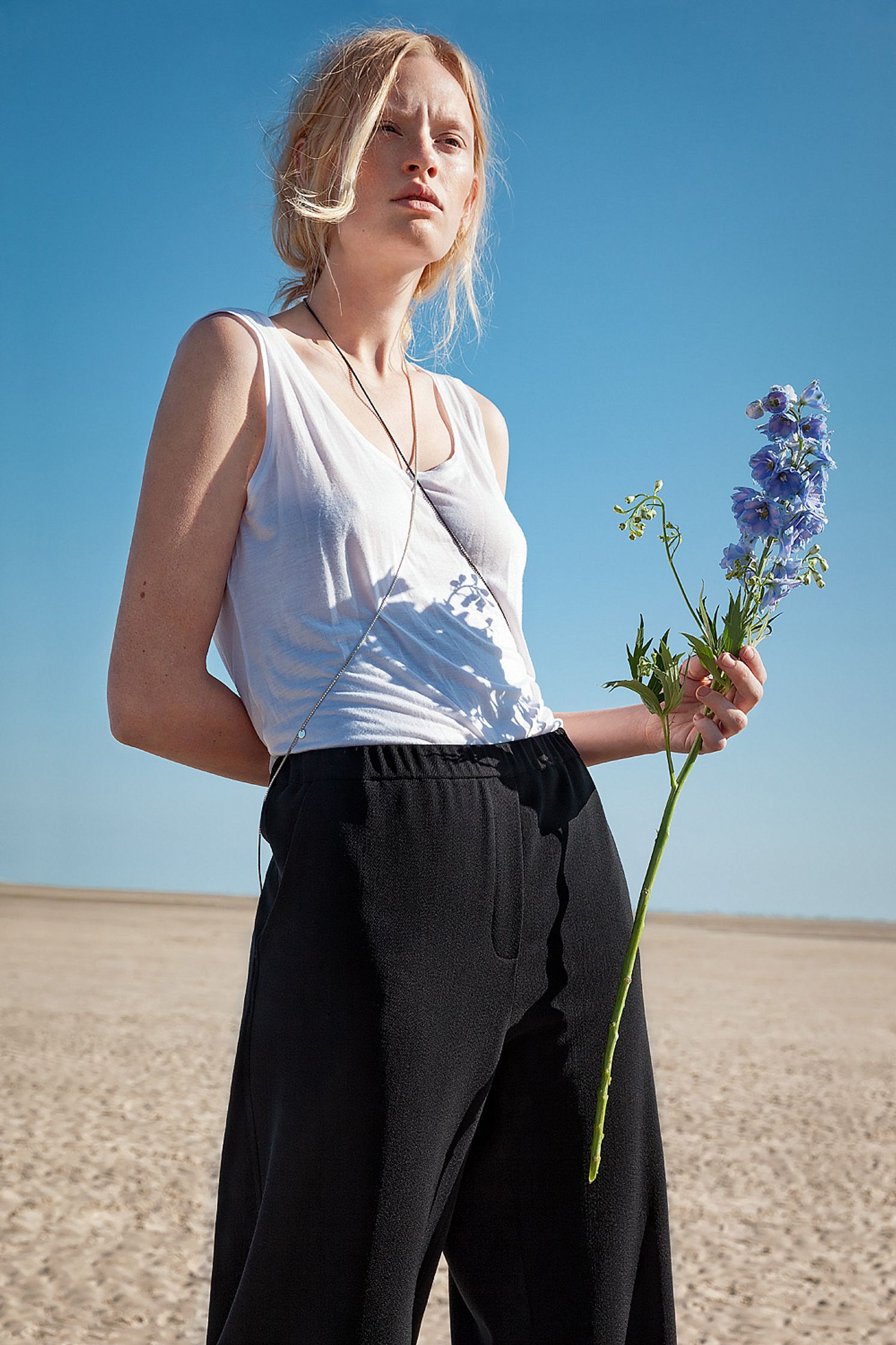 a woman in a white top and black pants standing on the beach  retouche advertising campaign