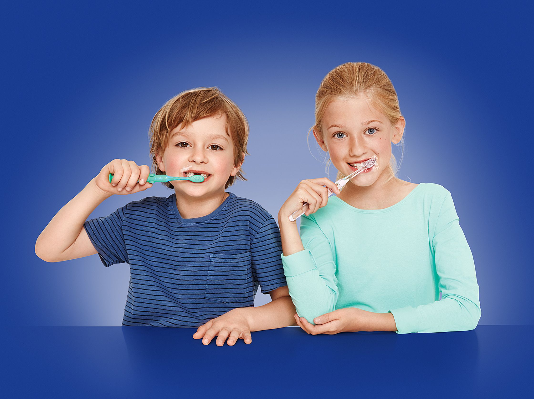 two children brushing their teeth in front of a blue background - Bildbearbeitung Hamburg