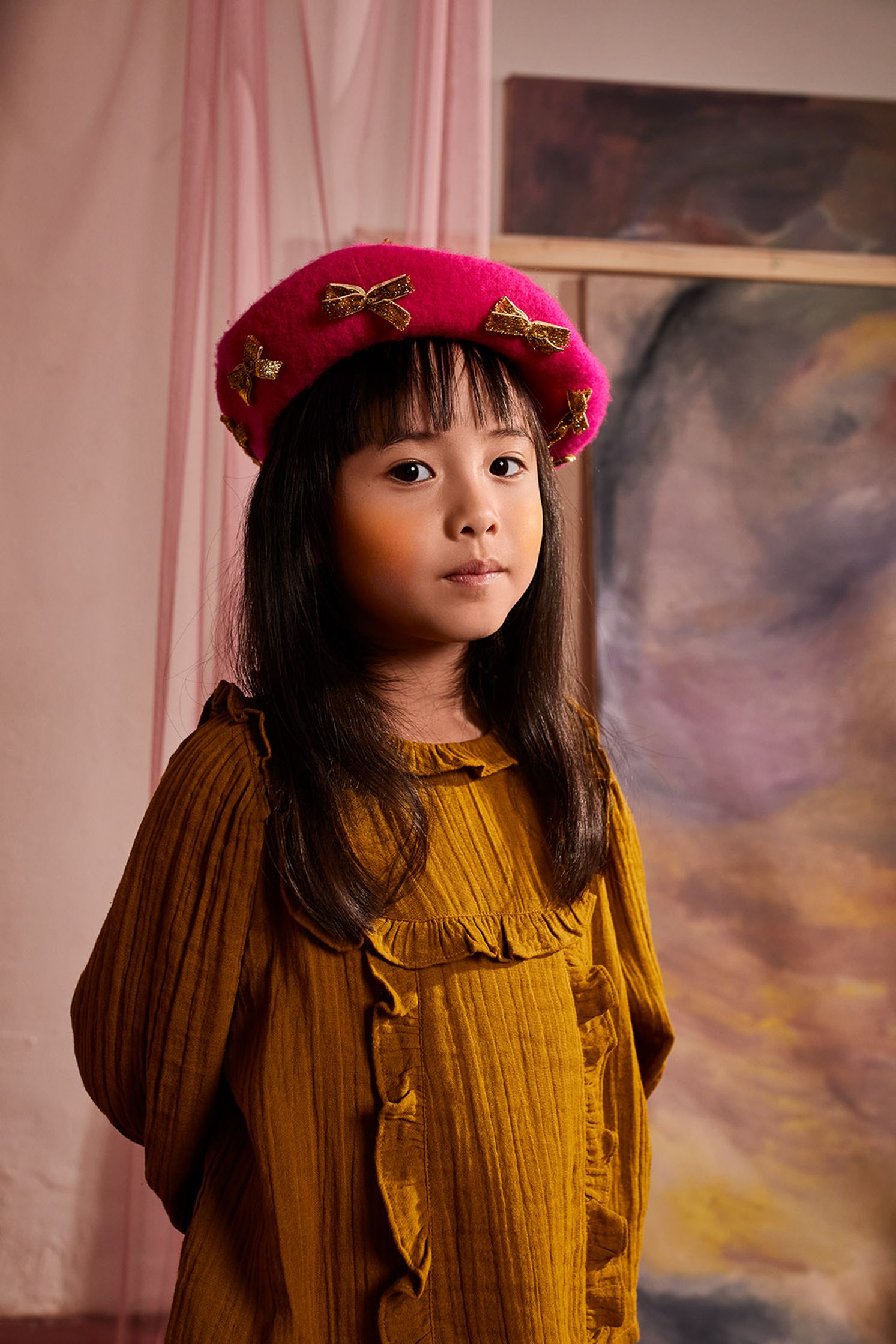 a little girl wearing a pink hat in front of a painting