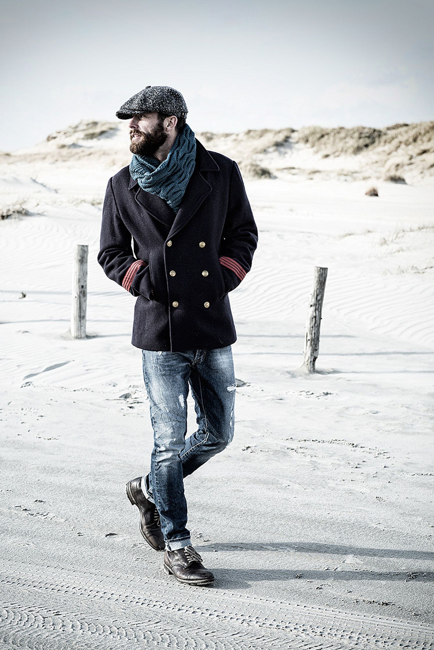 a bearded man wearing a hat and jeans on the beach retusche bildbearbeitung