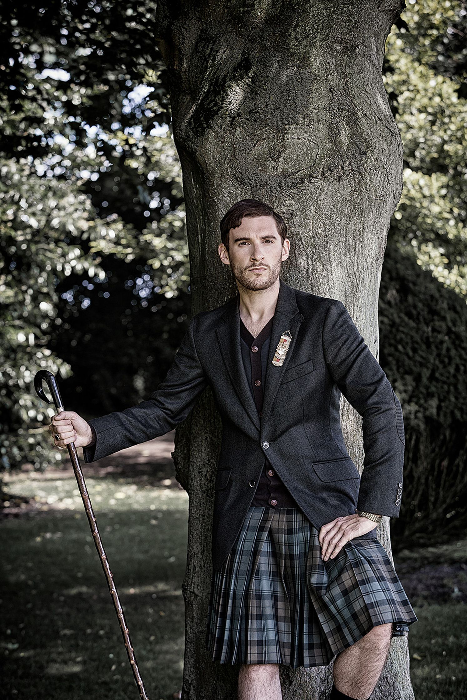 a man in a kilt leaning against a tree creative post production