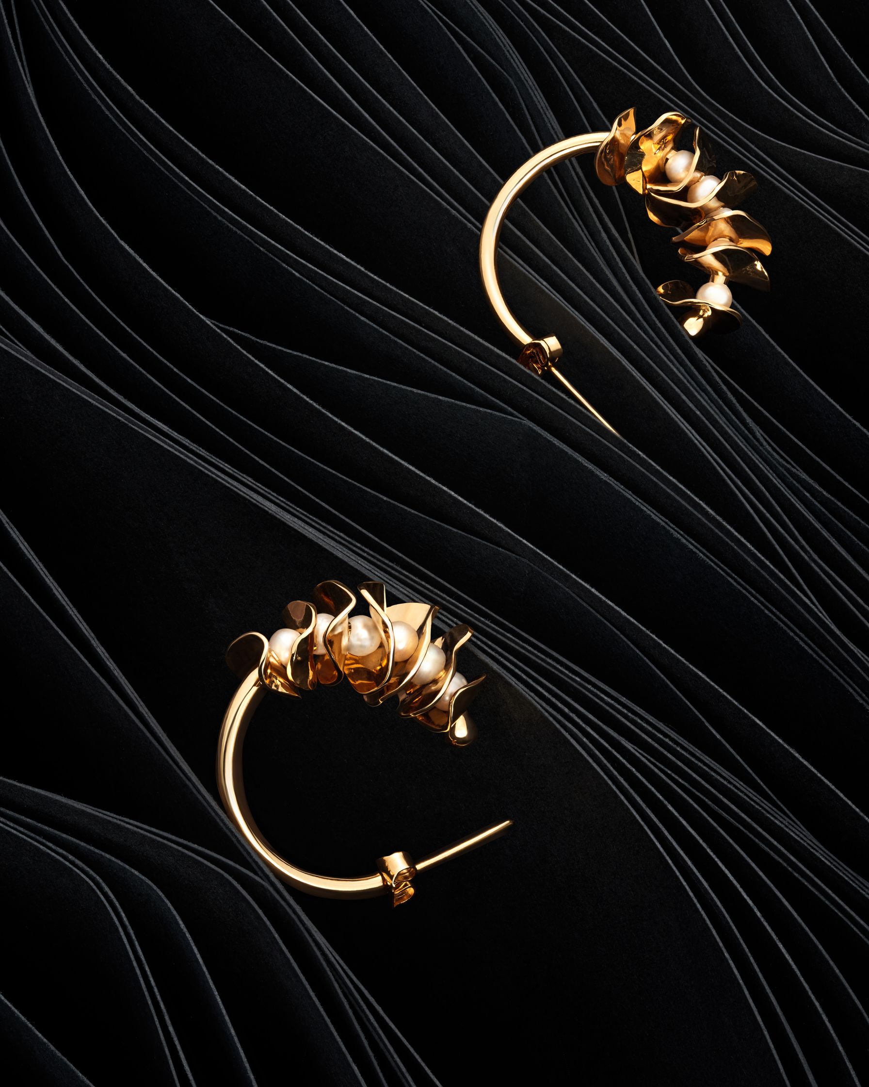 Pair of gold earrings by Lisa Motte, styled on black paper waves, representing organic leaf shapes.