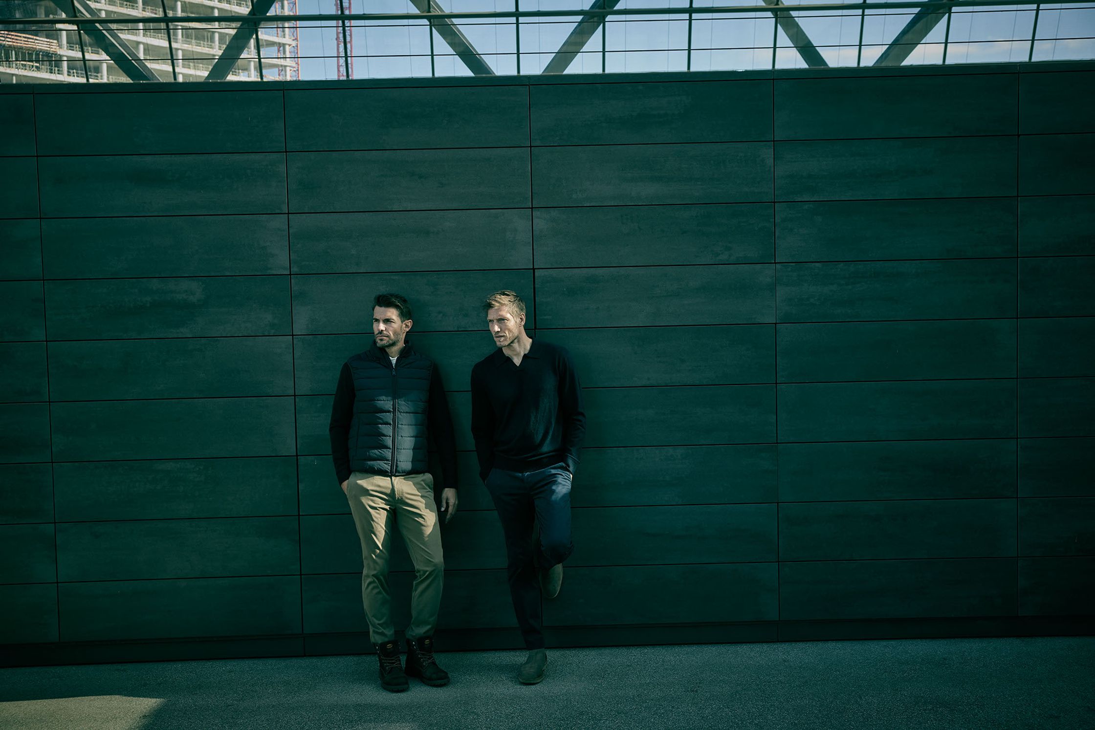 two men leaning against a wall in front of a building