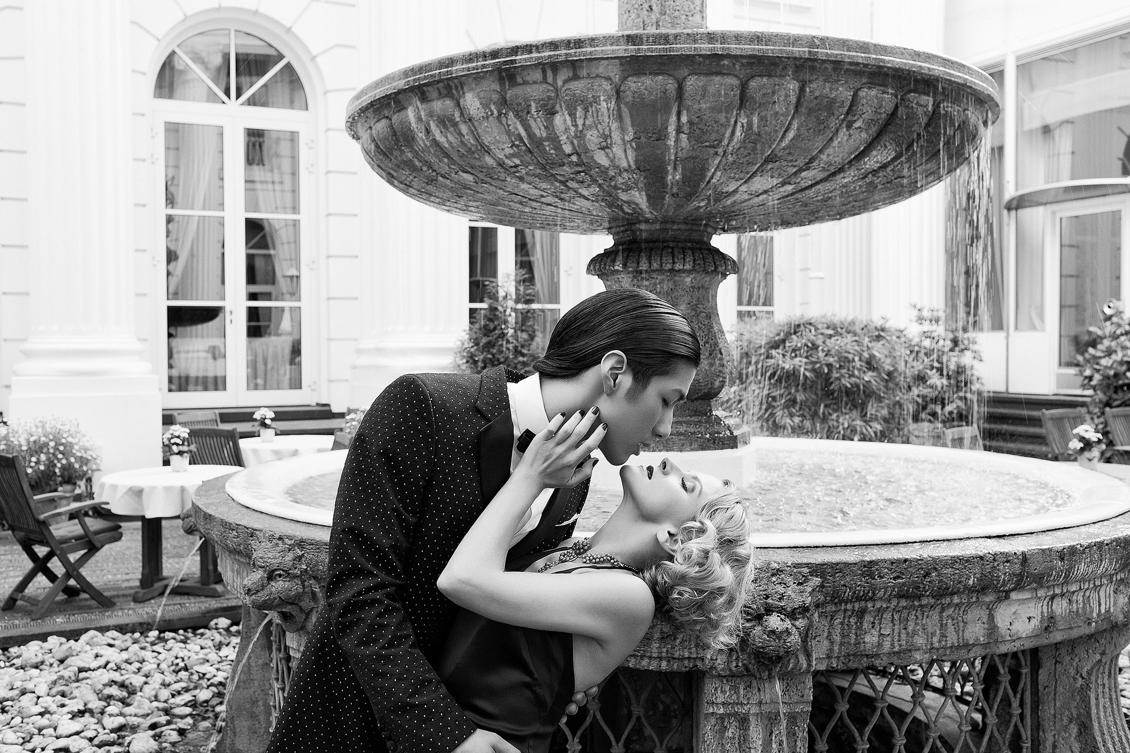 a black and white photo of a couple kissing in front of a fountain advertising retouch hamburg