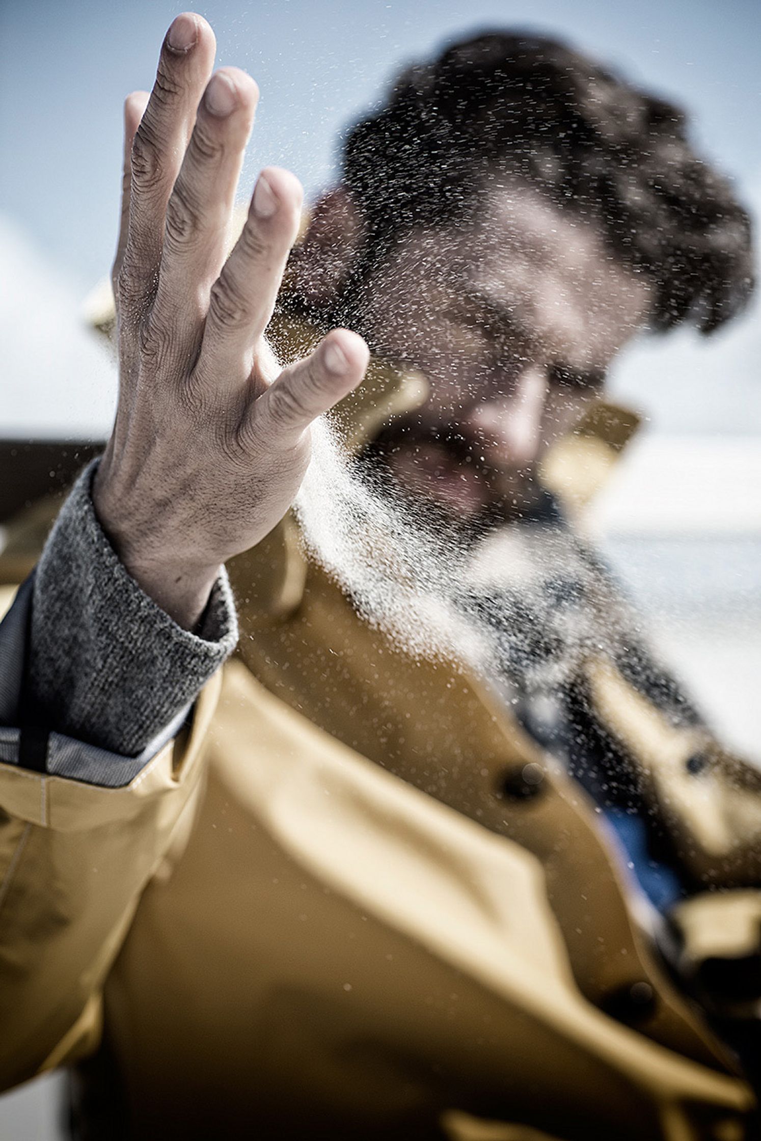 a man in a yellow jacket is sprinkling sand on his hand retusche image campaign