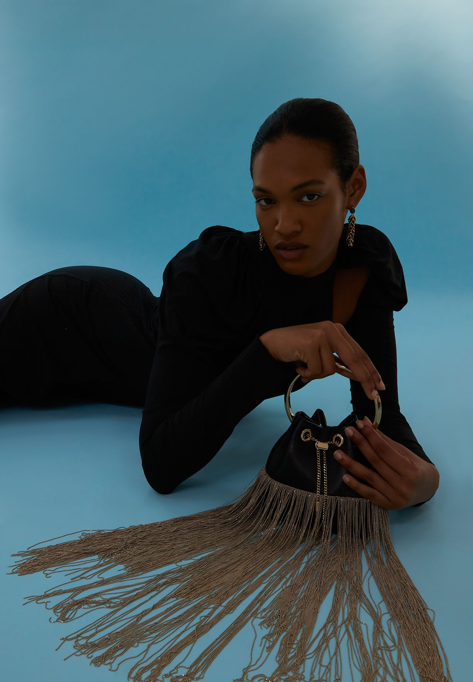 a woman laying on a blue background with a fringed bag