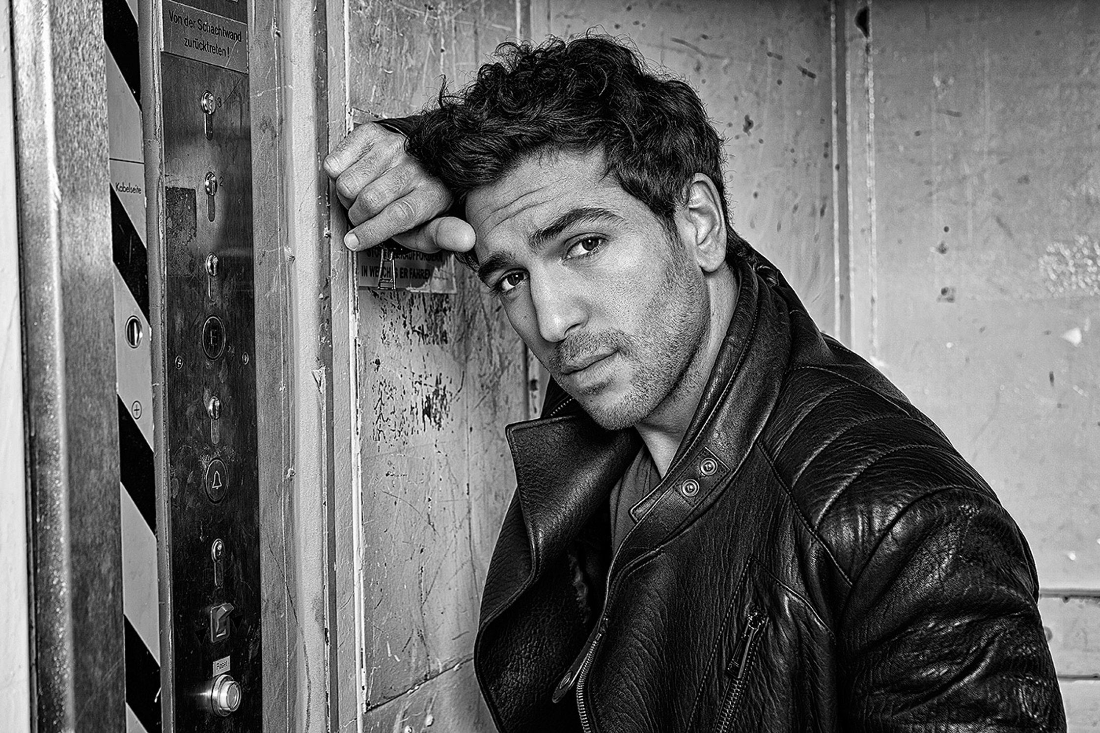 elyas m'barek in a leather jacket leaning against a wall
retusche by glamtouch